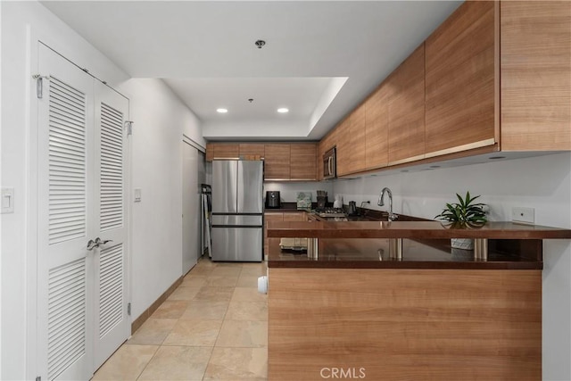 3785 Wilshire Blvd Unit 1605, Los Angeles, CA 90010 - kitchen featuring appliances with stainless steel finishes, dark countertops, brown cabinetry, a peninsula, and recessed lighting