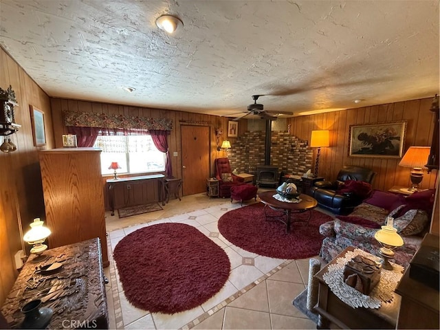 59663 Sunway Dr, Yucca Valley, CA 92284 - living area with tile patterned floors, wooden walls, a wood stove, a ceiling fan, and a textured ceiling