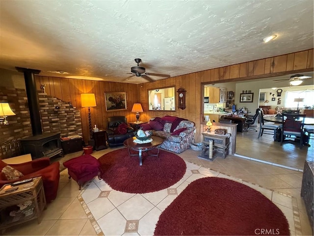 59663 Sunway Dr, Yucca Valley, CA 92284 - living room with a ceiling fan, light tile patterned flooring, a wood stove, wood walls, and a textured ceiling