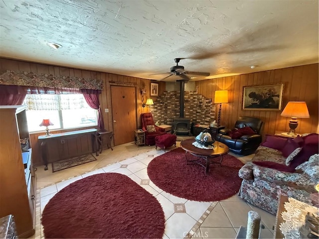 59663 Sunway Dr, Yucca Valley, CA 92284 - living area with light tile patterned floors, a wood stove, wooden walls, and ceiling fan