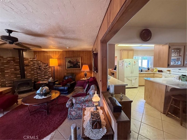 59663 Sunway Dr, Yucca Valley, CA 92284 - living room featuring light tile patterned floors, a wood stove, a ceiling fan, a textured ceiling, and wood walls