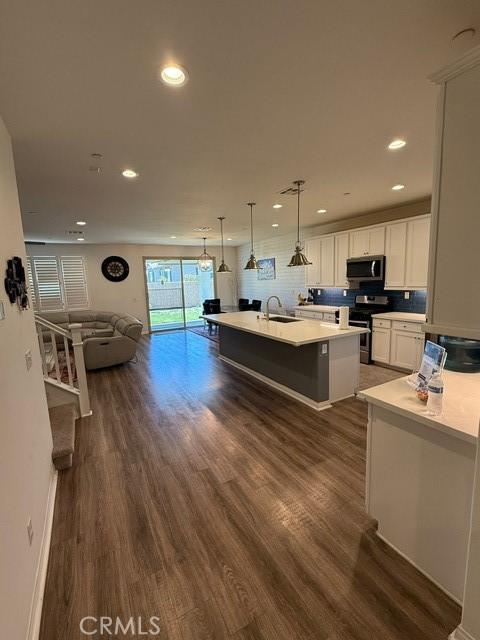 16009 Pitzer St, Fontana, CA 92336 - kitchen featuring appliances with stainless steel finishes, open floor plan, dark wood-style floors, a kitchen island with sink, and white cabinetry