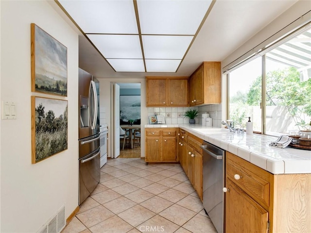 9386 Cambridge St, Cypress, CA 90630 - kitchen with stainless steel appliances, light tile patterned floors, backsplash, brown cabinetry, and tile counters