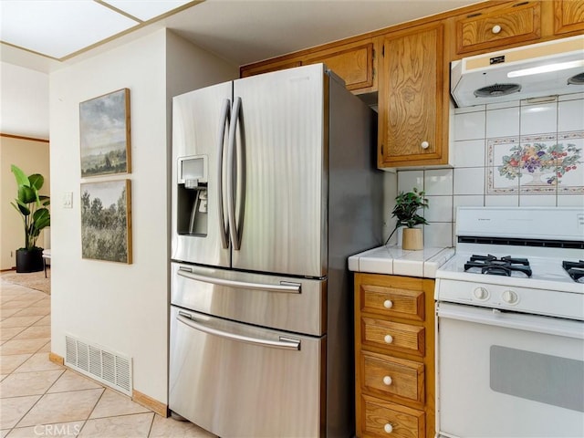 9386 Cambridge St, Cypress, CA 90630 - kitchen featuring stainless steel refrigerator with ice dispenser, white range with gas cooktop, under cabinet range hood, tile countertops, and decorative backsplash