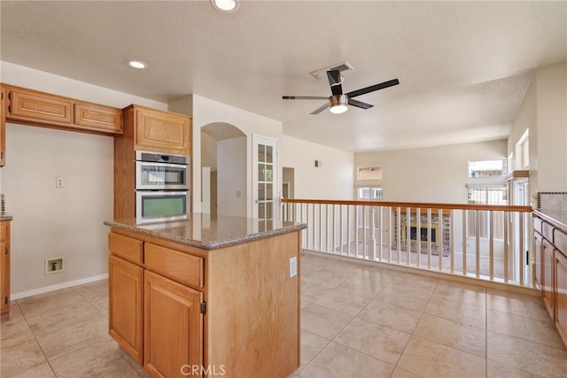 15280 Dunes Way, Moreno Valley, CA 92555 - kitchen with stainless steel double oven, a ceiling fan, a center island, stone counters, and light tile patterned floors