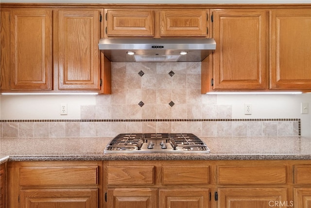 15280 Dunes Way, Moreno Valley, CA 92555 - kitchen featuring under cabinet range hood, stainless steel gas cooktop, backsplash, stone counters, and brown cabinetry