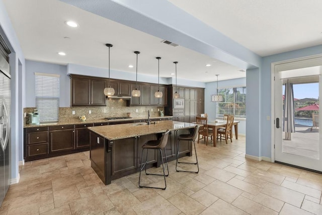 11550 Carowind Ln, Scripps Miramar, CA 92131 - kitchen featuring dark brown cabinets, backsplash, stainless steel gas cooktop, light stone counters, and a breakfast bar