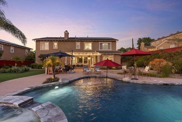 11550 Carowind Ln, Scripps Miramar, CA 92131 - back of house at dusk featuring a patio, roof mounted solar panels, outdoor dining area, an outdoor pool, and a chimney