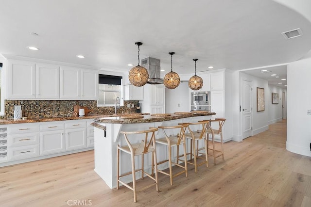 516 S The Strand # A, Oceanside, CA 92054 - kitchen with stainless steel microwave, light wood-type flooring, a center island, white cabinetry, and recessed lighting