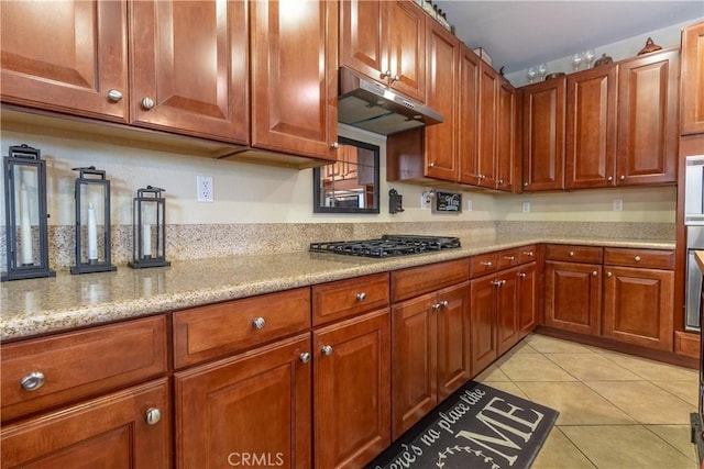 2168 Stonewood St, Mentone, CA 92359 - kitchen with stainless steel gas cooktop, under cabinet range hood, light tile patterned floors, light stone counters, and brown cabinetry