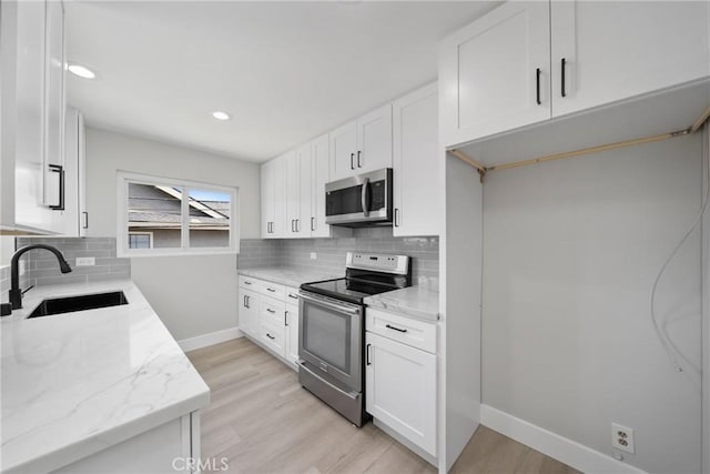 503 Saint Andrews Rd Unit E, Newport Beach, CA 92663 - kitchen with stainless steel appliances, decorative backsplash, light stone countertops, light wood-style floors, and white cabinetry