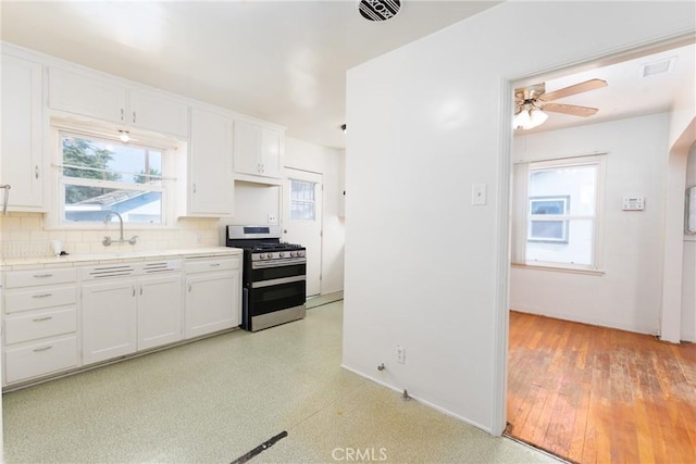 7086 Fairfax Dr, San Bernardino, CA 92404 - kitchen with stainless steel gas stove, white cabinets, decorative backsplash, tile counters, and plenty of natural light