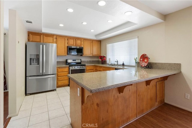 6879 Mission Grove Pkwy N, Riverside, CA 92506 - kitchen featuring stainless steel appliances, a peninsula, a tray ceiling, recessed lighting, and a kitchen bar