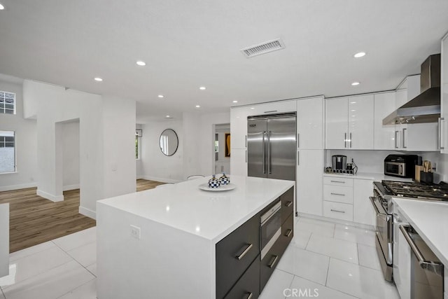 24523 Via Esquina, Calabasas, CA 91302 - kitchen featuring wall chimney range hood, built in appliances, modern cabinets, light countertops, and white cabinetry
