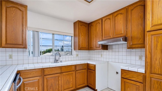 2116 Marine Ave, Gardena, CA 90249 - kitchen with under cabinet range hood, brown cabinetry, tasteful backsplash, and tile counters
