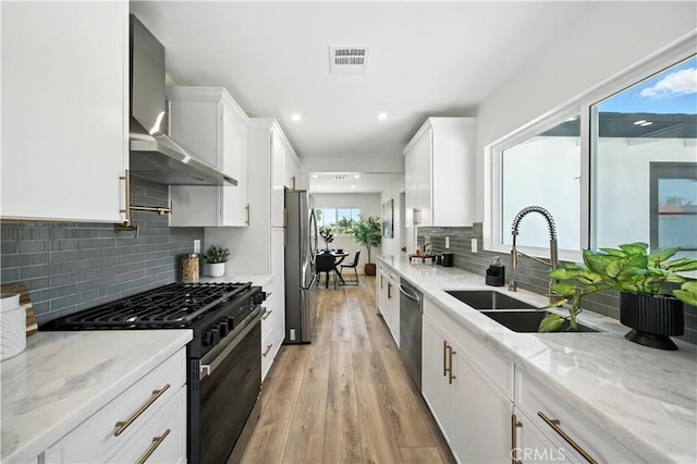 5243 Tara Pl, San Diego, CA 92117 - kitchen featuring stainless steel appliances, wall chimney exhaust hood, white cabinetry, light wood finished floors, and light stone counters
