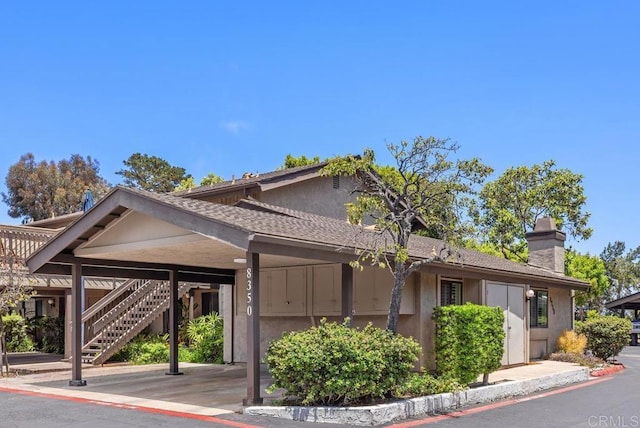 8350 Via Sonoma Unit A, La Jolla, CA 92037 - view of front facade featuring stairway, a chimney, stucco siding, covered parking, and a shingled roof