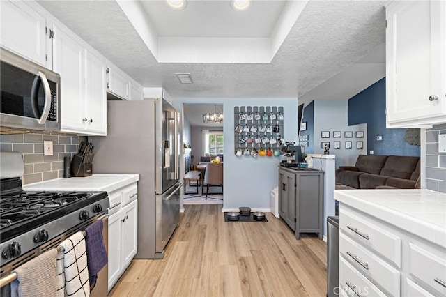 13220 February Dr, Corona, CA 92879 - kitchen with appliances with stainless steel finishes, light wood-style flooring, tile counters, white cabinets, and a textured ceiling