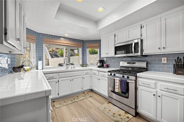 13220 February Dr, Corona, CA 92879 - kitchen with stainless steel appliances, tile countertops, white cabinetry, recessed lighting, and a textured ceiling