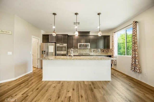 1920 Clementine St, Redlands, CA 92374 - kitchen featuring appliances with stainless steel finishes, a center island with sink, tasteful backsplash, light wood finished floors, and light stone countertops