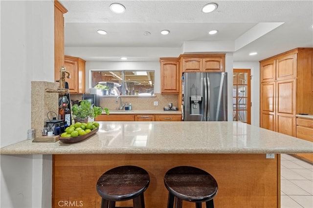 18229 Strathern St, Reseda, CA 91335 - kitchen with stainless steel fridge, a peninsula, a breakfast bar area, light tile patterned floors, and light stone countertops