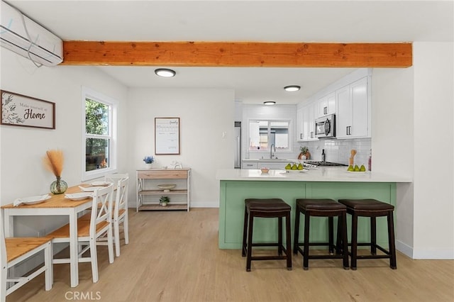 2998 N H St, San Bernardino, CA 92405 - kitchen featuring stainless steel appliances, a wall unit AC, beam ceiling, light wood-style floors, and white cabinetry