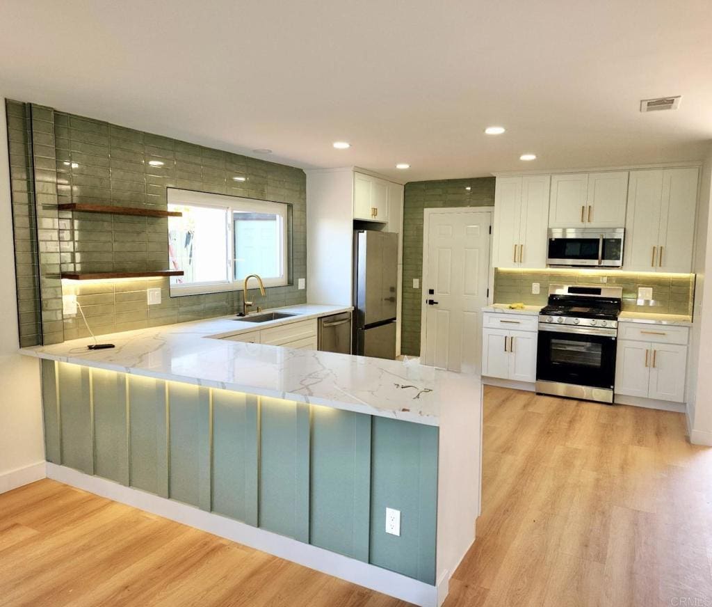2819 Morningside St, San Diego, CA 92139 - kitchen with appliances with stainless steel finishes, white cabinets, tasteful backsplash, light wood-style floors, and light stone countertops