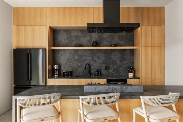 60632 Granville Rd, Joshua Tree, CA 92252 - kitchen with wall chimney exhaust hood, high end refrigerator, modern cabinets, dark countertops, and a kitchen breakfast bar