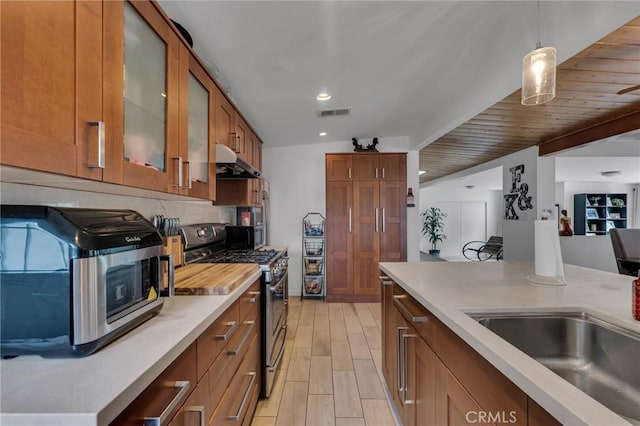 9707 Foothill Blvd, Sylmar, CA 91342 - kitchen with stainless steel appliances, under cabinet range hood, brown cabinets, light countertops, and glass insert cabinets