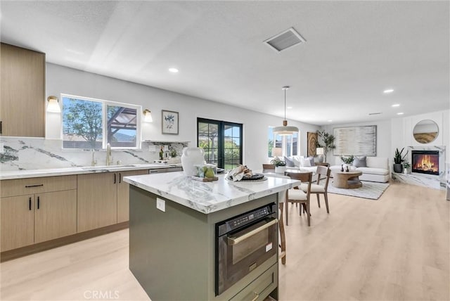 46079 Galaxy Ct, Temecula, CA 92592 - kitchen with light wood-style flooring, open floor plan, recessed lighting, tasteful backsplash, and a glass covered fireplace