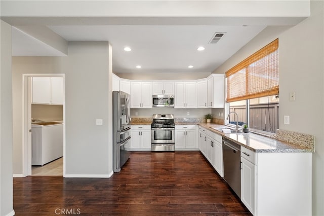 45114 Via Quivera, Temecula, CA 92592 - kitchen featuring appliances with stainless steel finishes, washer / dryer, white cabinetry, light stone countertops, and dark wood-style floors