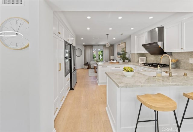 6 Baristo Unit 39, Irvine, CA 92612 - kitchen featuring wall chimney exhaust hood, a peninsula, light wood-style flooring, white cabinets, and recessed lighting