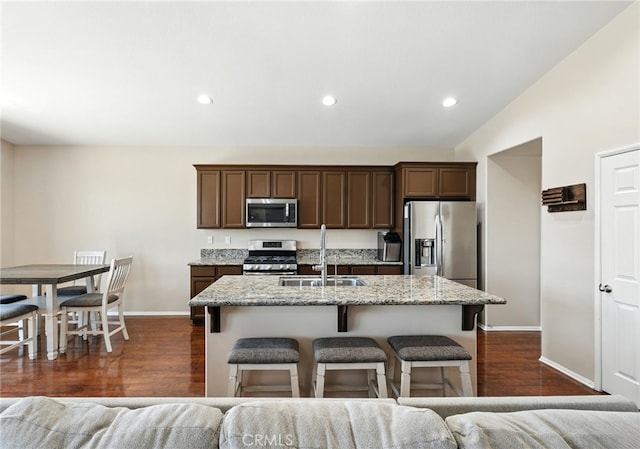 31969 Frontier Manor St, Menifee, CA 92584 - kitchen featuring stainless steel appliances, dark wood finished floors, a kitchen island with sink, light stone counters, and a breakfast bar