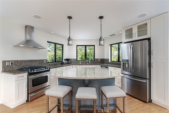 125 Park Pl, Pismo Beach, CA 93449 - kitchen featuring wall chimney exhaust hood, appliances with stainless steel finishes, a breakfast bar area, light stone counters, and light wood finished floors