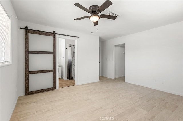 7573 Cibola Trl, Yucca Valley, CA 92284 - unfurnished bedroom featuring light wood-style floors, a barn door, a ceiling fan, and ensuite bath