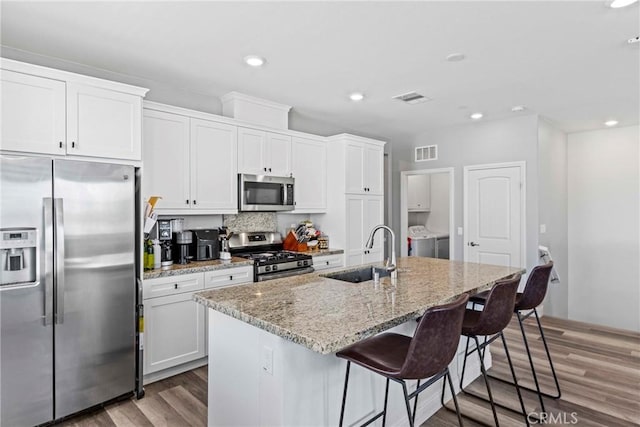 7020 Turin Pl, Eastvale, CA 92880 - kitchen featuring appliances with stainless steel finishes, light wood-type flooring, a center island with sink, a kitchen bar, and light stone counters