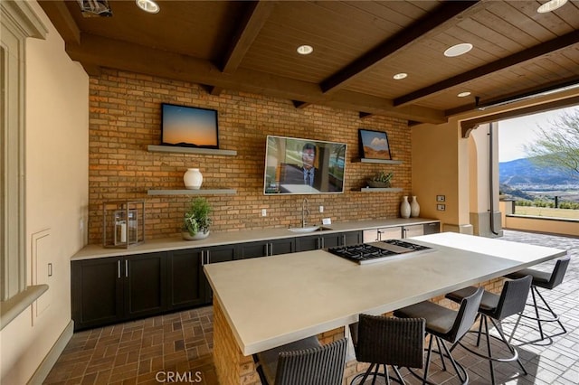 24185 Sprout Dr, Corona, CA 92883 - kitchen featuring stainless steel gas cooktop, brick patterned flooring, open shelves, a breakfast bar, and a wooden ceiling with exposed beams
