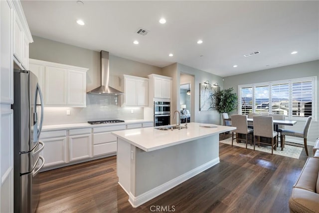 24185 Sprout Dr, Corona, CA 92883 - kitchen with wall chimney range hood, appliances with stainless steel finishes, white cabinetry, decorative backsplash, and dark wood finished floors