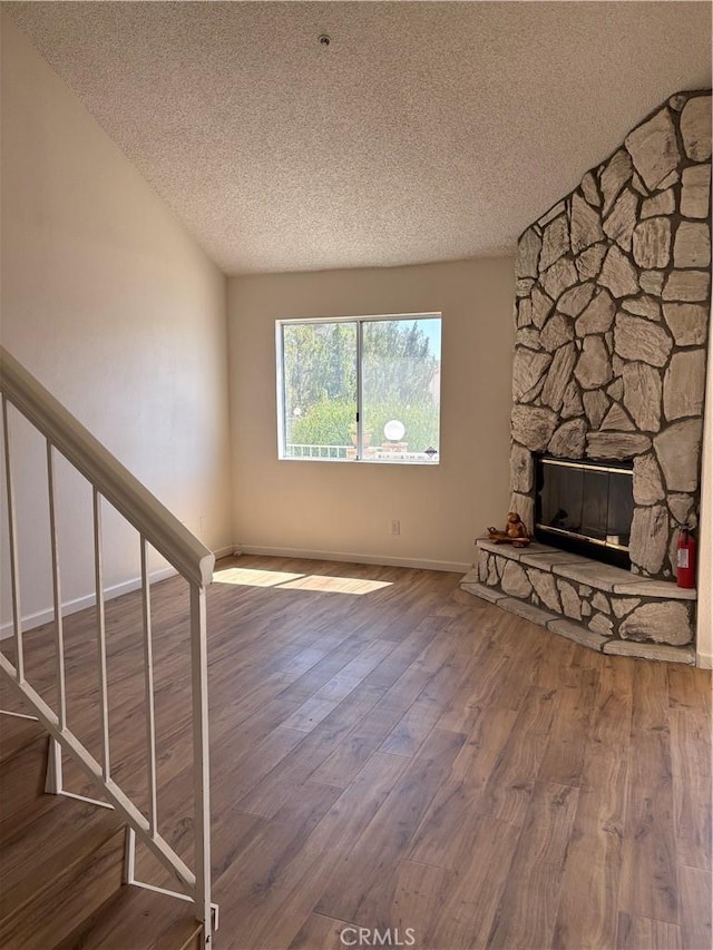 11496 Nautical Ln Unit 19, Helendale, CA 92342 - unfurnished living room featuring a textured ceiling, wood finished floors, stairs, a stone fireplace, and vaulted ceiling