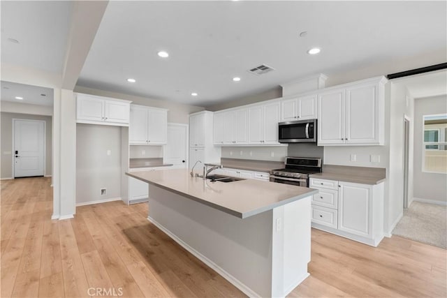 30071 Merrick Ln, Menifee, CA 92584 - kitchen with stainless steel appliances, a center island with sink, white cabinets, light wood-style floors, and recessed lighting