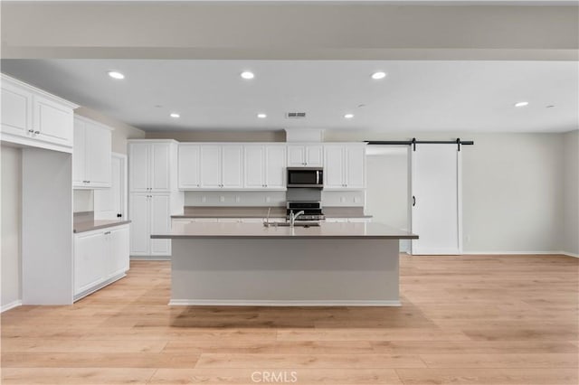 30071 Merrick Ln, Menifee, CA 92584 - kitchen with stainless steel microwave, white cabinetry, an island with sink, recessed lighting, and light wood-style flooring