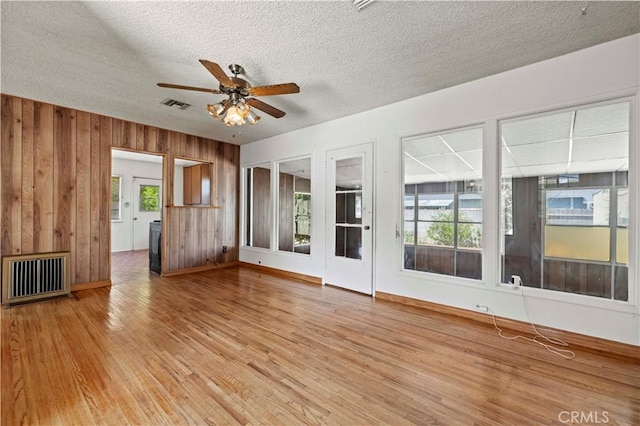 7737 Nestle Ave, Reseda, CA 91335 - unfurnished living room featuring ceiling fan, light wood-type flooring, healthy amount of natural light, wood walls, and a textured ceiling