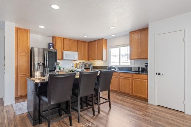 14075 Tourmaline St, Hesperia, CA 92344 - kitchen featuring stainless steel refrigerator with ice dispenser, white microwave, a kitchen bar, light wood-type flooring, and recessed lighting