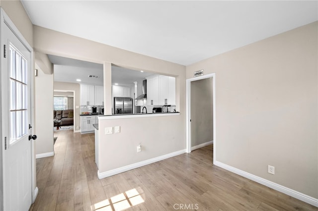 2729 Fairman St, Lakewood, CA 90712 - kitchen featuring stainless steel refrigerator with ice dispenser, white cabinetry, light wood finished floors, wall chimney range hood, and a peninsula