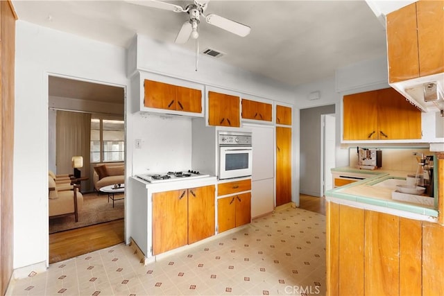 1450 Pepper Tree Ln, San Bernardino, CA 92404 - kitchen featuring white appliances, light floors, ceiling fan, brown cabinetry, and tile countertops