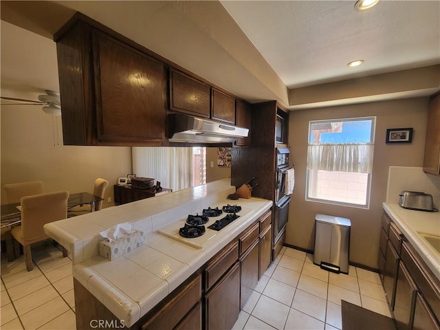 13224 Greenstone Ave, Norwalk, CA 90650 - kitchen with tile counters, white gas cooktop, under cabinet range hood, dark brown cabinetry, and light tile patterned flooring