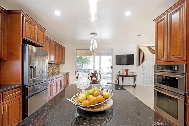 22329 Plummer St, Chatsworth, CA 91311 - kitchen featuring appliances with stainless steel finishes, decorative backsplash, brown cabinetry, dark stone countertops, and hanging light fixtures