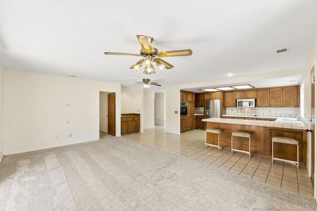 2239 Sunset Dr, Escondido, CA 92025 - kitchen featuring appliances with stainless steel finishes, brown cabinetry, tile countertops, a peninsula, and a breakfast bar area
