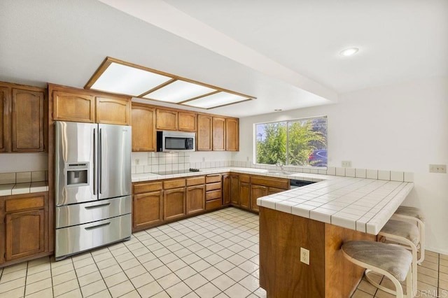 2239 Sunset Dr, Escondido, CA 92025 - kitchen with appliances with stainless steel finishes, a peninsula, brown cabinetry, light tile patterned floors, and tasteful backsplash