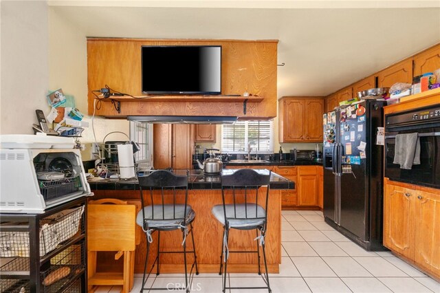 19722 Tajauta Ave, Carson, CA 90746 - kitchen with black appliances, a breakfast bar area, a peninsula, dark countertops, and light tile patterned floors